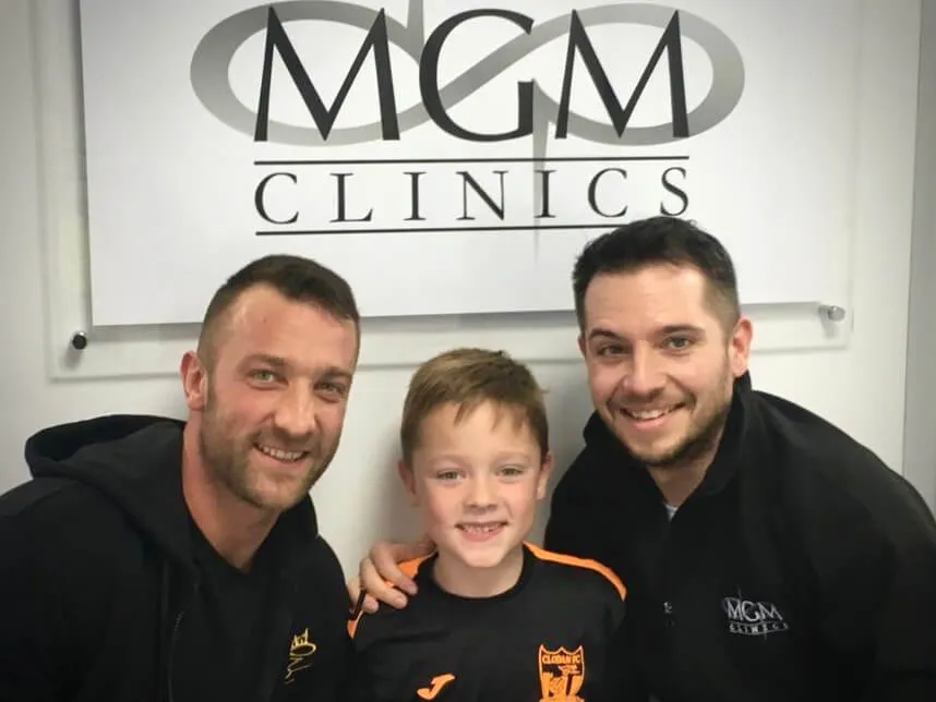 Two MGM Clinics practitioners with a young patient in front of the clinic logo